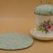 This shows the pincushion bobbin holder next to the trivet. The trivet is about 5.5 inches wide. Flower is on saucer to left of cup. This shows the pincushion bobbin holder next to the trivet. The trivet is about 5.5 inches wide. Flower is on saucer to left of cup.